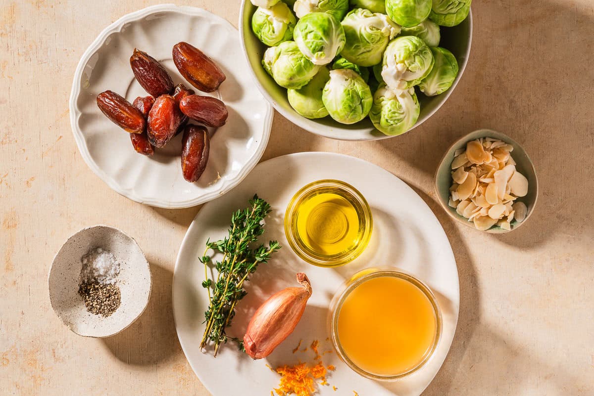 Ingredients for roasted brussels sprouts including brussels sprouts, sliced almonds, olive oil, salt, black pepper, apple cidar vinegar, grated orange zest, fresh thyme, shallot, and dates.