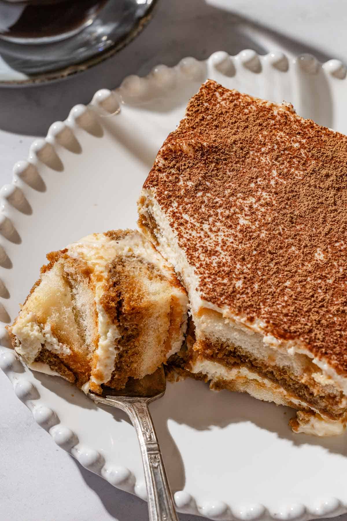 A close up of a slice of tiramisu on a plate with a fork.